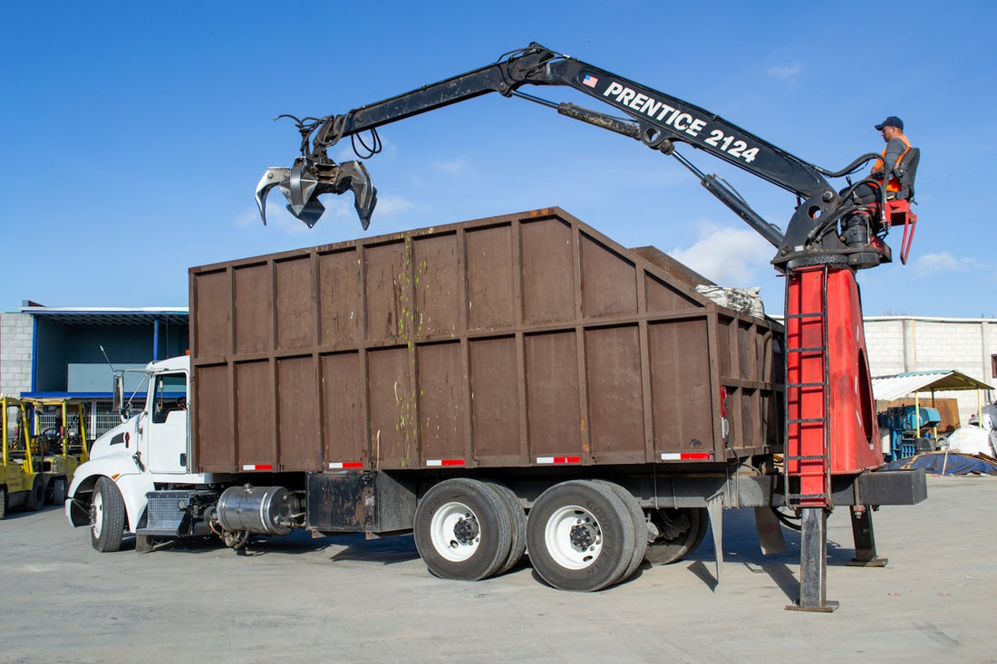 Crane truck loading debris into a large bin.