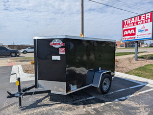 Black cargo trailer with 'Cargo Mate' branding parked in a lot with a trailer sales sign in the background.