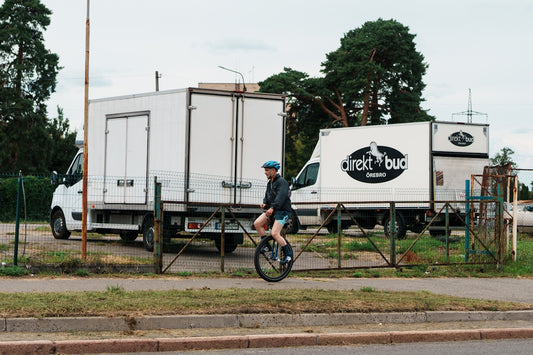 Man rides unicycle past parked white trucks
