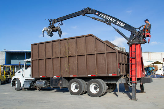 Crane truck loading debris into a large bin.
