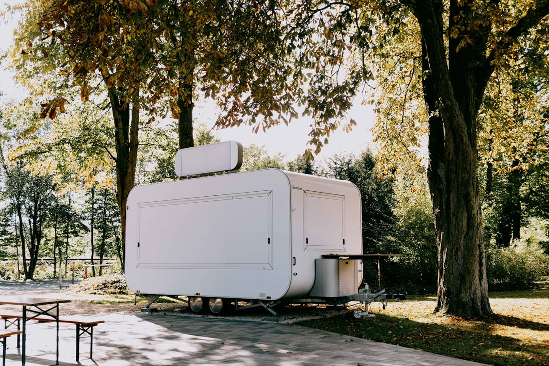 A white food trailer parked under trees