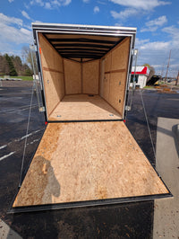 Rear view of 2026 Cargo Mate E-Series 7x14 enclosed cargo trailer with ramp door fully lowered showing 3/4 inch engineered wood floor, 3/8 inch engineered wood walls with 16 inch on-center studs, and aluminum wrap with ATP