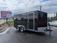 2026 Cargo Mate E-Series 7x14 tandem axle enclosed cargo trailer in black with 6 inch extra height, 32 inch RV side door, rear ramp door, and 24 inch aluminum tread plate stoneguard — front curbside angle at AAA Trailer in Howell Michigan