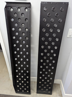 A pair of heavy duty steel loading ramps with a black powdercoat finish and multiple circular cutouts for traction.