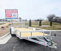 A Silver Ox tandem axle aluminum utility trailer with wooden decking and a rear ramp, displayed at a dealership lot.