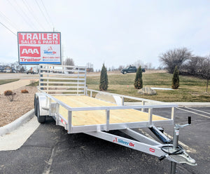A Silver Ox tandem axle aluminum utility trailer with wooden decking and a rear ramp, displayed at a dealership lot.
