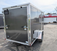 A 2025 Amerilite 6x12 Aluminum Enclosed Trailer with Ramp Door, displayed in a commercial setting with other vehicles in the background.