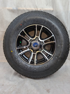 A 15 inch aluminum trailer wheel with a black and silver finish, mounted with a radial tire.