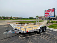 Silver OX Aluminum utility trailer parked in a lot with a trailer sales and parts sign in the background.