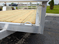 Wooden trailer deck on a metal frame with a grassy area and vehicles in the background.