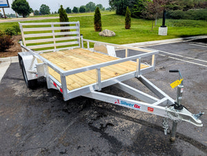 Silver Ox Aluminum utility trailer with wooden bed on a paved surface, surrounded by grass and trees.