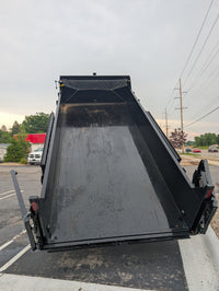 Black dump trailer on a street with vehicles and trees in the background