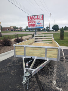 Aluminum Framed wood side utility trailer parked in a lot with a 'Trailer Sales & Parts' sign in the background.