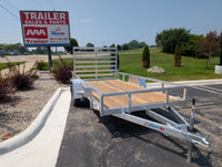 Silver Ox Aluminum trailer with wooden platform on a paved road, with 'Trailer Sales and Parts' sign in the background.