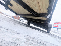 Trailer bed with wooden floor on a snowy road, with a building and sign in the background.
