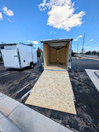 2026 AmeraLite Storm 6x10 Black — ramp door fully deployed showing full interior cargo area, OSB floor and walls | White unit visible in background